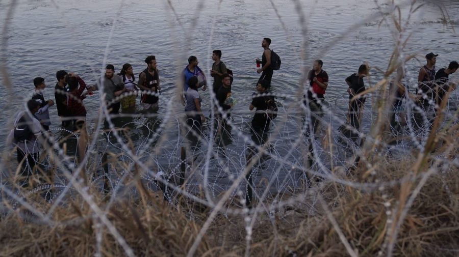 FILE - Migrants wait to climb over concertina wire after they crossed the Rio Grande and entered the U.S. from Mexico, Saturday, Sept. 23, 2023, in Eagle Pass, Texas. Abbott is expected to sign into law sweeping new powers that allow police to arrest migrants who cross the border illegally and gives local judges authority to order them to leave the country. (AP Photo/Eric Gay, File)