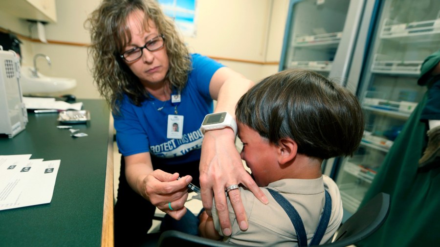 A nurse administers a vaccine into the arm of a child.