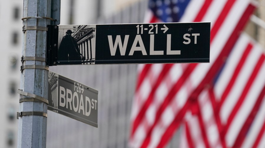 A Wall Street sign is seen in front of an American flag.