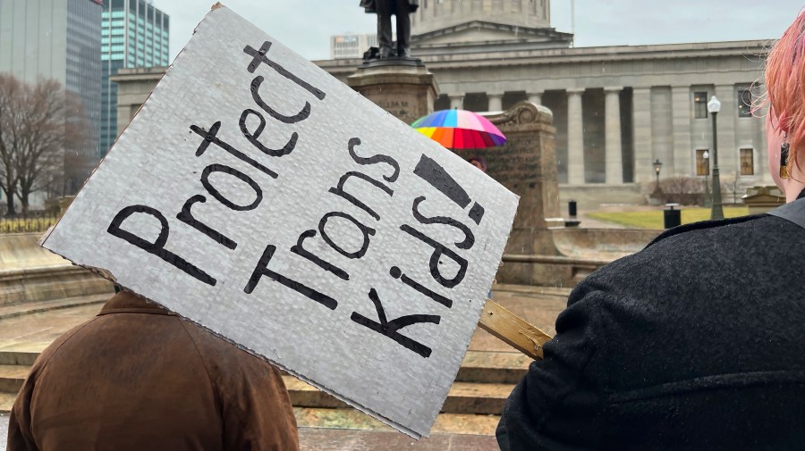 Protesters advocating for transgender rights and health care hold up signs outside the Ohio Statehouse.