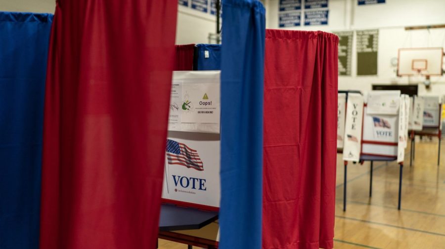 Red and blue curtains separate voting booths set up in a high school gym.