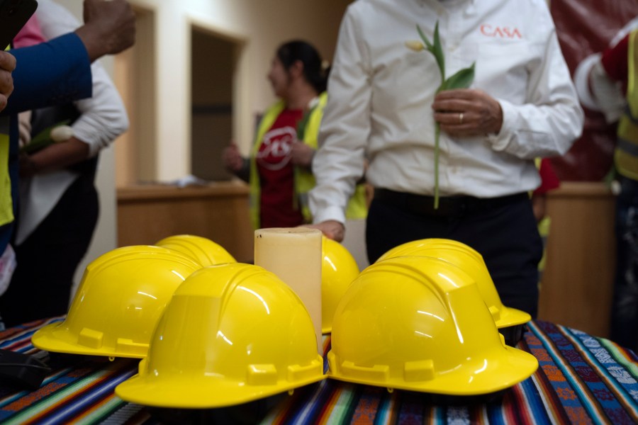 Construction workers and supporters gather around six construction helmets and a candle at a vigil and press conference by CASA of Maryland, a community advocacy group, to remember the six workers killed in the collapse of the Francis Scott Key Bridge and to highlight the difficult conditions faced by immigrant construction workers on Friday, March 29, 2024, in Baltimore, Md. (AP Photo/Mark Schiefelbein)