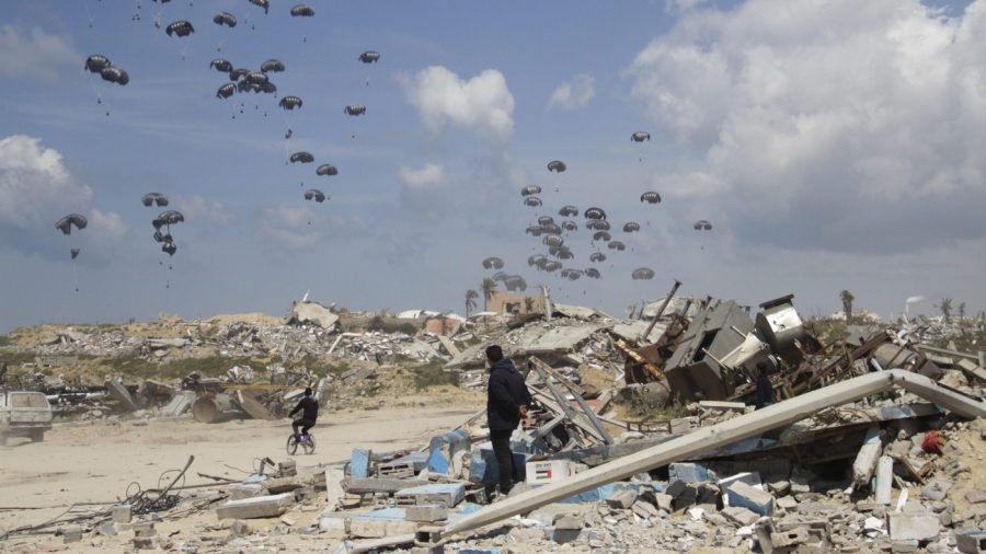 Onlookers observing from an area covered in debris and rubble watch as parachutes containing humanitarian aid float down over part of Gaza City.