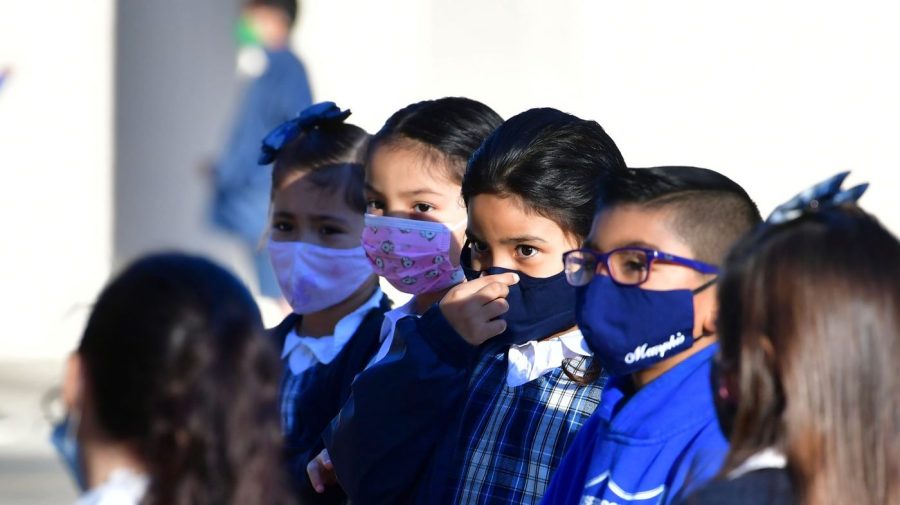 Children standing in a school yard all wearing face masks.