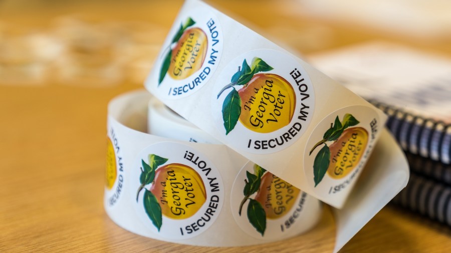 A roll of stickers displaying a peach with the words "I'm a Georgia Voter" on top are shown on a table.