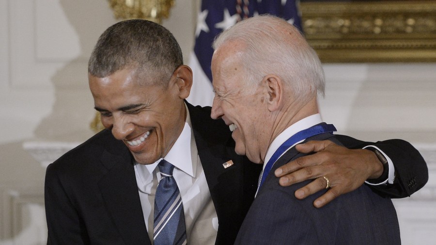 President Obama and Vice President Biden laugh while embracing at a ceremony.