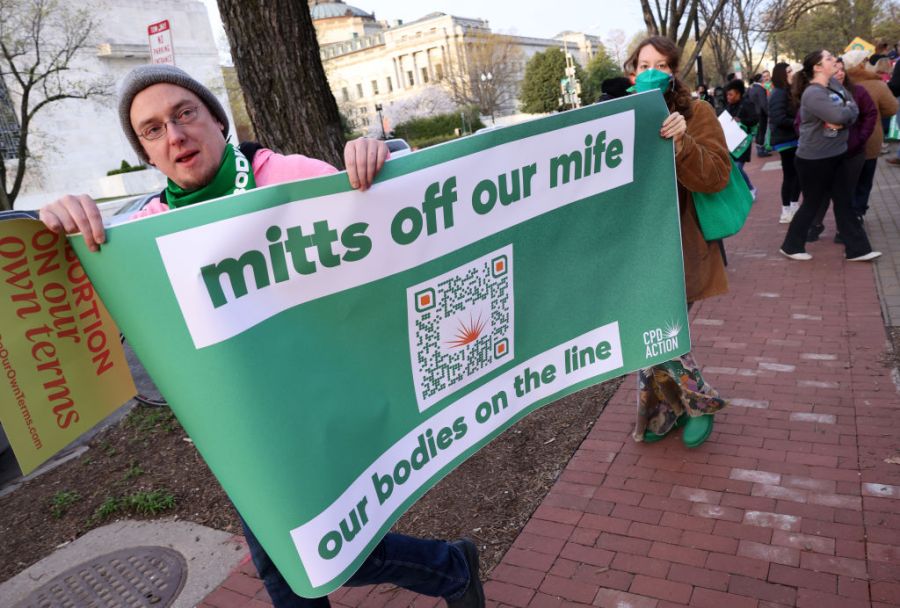 Demonstrators march toward the Capitol carrying a large sign.