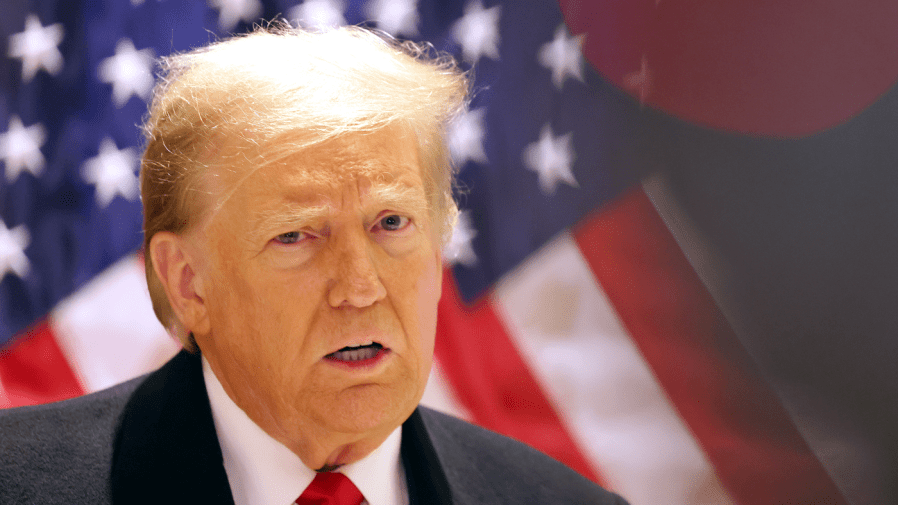 Former President Trump speaks during a press conference in front of an American flag.