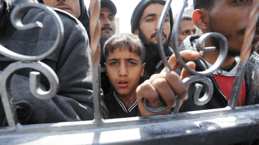 Palestinians line up against a gate.