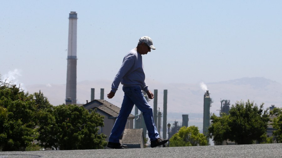 In this July 12, 2017 file photo the stacks from the Valero Benicia Refinery are seen as a pedestrian walks in a nearby neighborhood, in Benicia, Calif.