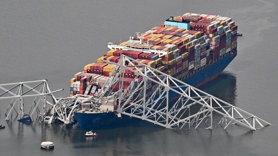 A damaged container ship rests next to a bridge pillar in the Patapsco River