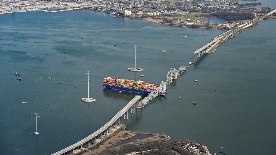 A damaged container ship rests next to a bridge pillar in the Patapsco River.