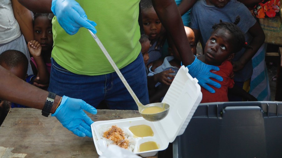 A server ladles soup into a container as children line up to receive food at a shelter for families displaced by gang violence, in Port-au-Prince, Haiti, Thursday, March 14, 2024.