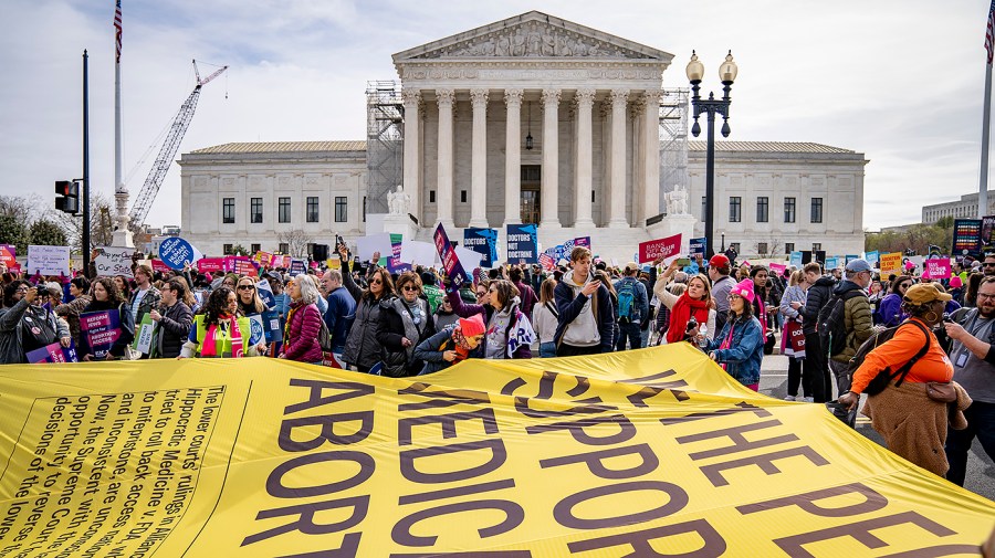 Supporters of abortion rights protest in front of the Supreme Court as organizers unravel a large poster.