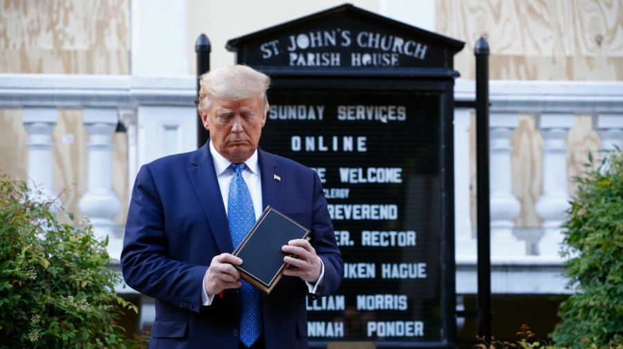 Former President Trump inspects a Bible he's holding while standing in front of a church sign.