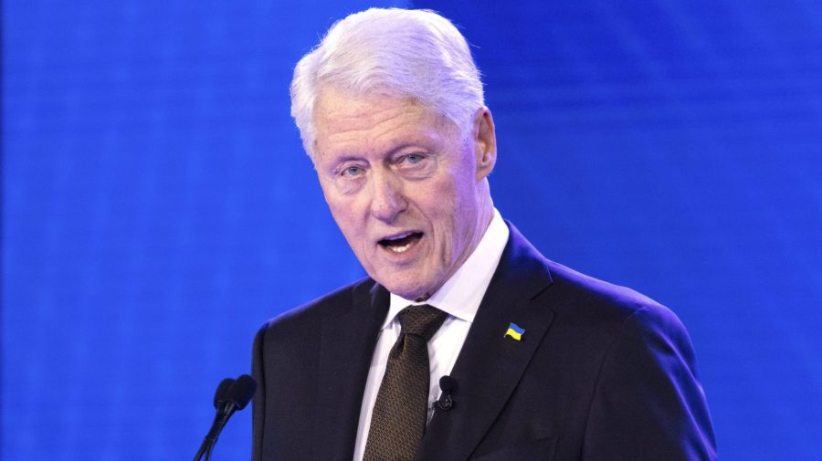 Former President Clinton speaks at an event against a bright blue backdrop.