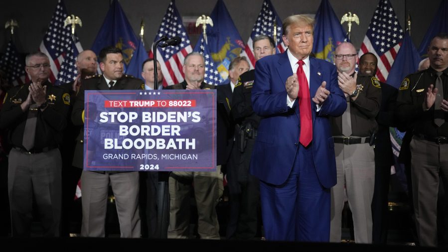 Former President Trump speaks at a campaign event next to a sign that reads "Stop Biden's Border Bloodbath."