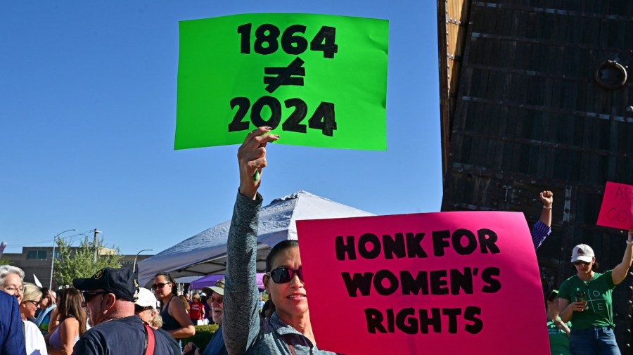 Abortion-rights demonstrators hold up signs that read "1864≠2024" and "Honk for Women's Rights" at a rally.