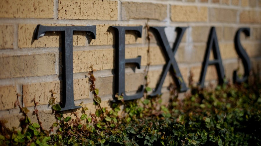 Letters spelling Texas are seen along a brick wall.