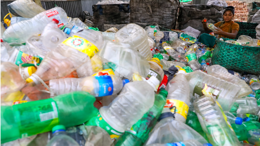 A woman works in a facility while surrounded by a pill of plastic bottles.