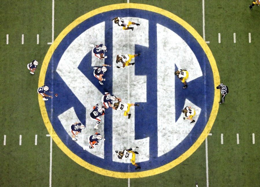 FILE - Auburn quarterback Nick Marshall (14), left, takes the snap from Auburn center Reese Dismukes (50) as the Auburn offense operates against Missouri on the SEC logo during the first half of Auburn's 59-42 win over Missouri in the SEC Championship at the Georgia Dome, Saturday, Dec. 7, 2013, in Atlanta, Ga. Southeastern Conference and Pac-12 officials are expected to provide the final approval of a $2.8 billion plan that will settle antitrust claims and set the stage for college athletes to start sharing the billions of dollars flowing to their schools. (AP Photo/Atlanta Journal-Constitution, Jason Getz, File)