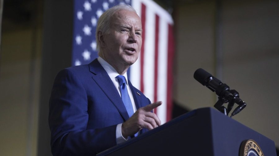 President Biden speaks into a microphone in front of an American flag.