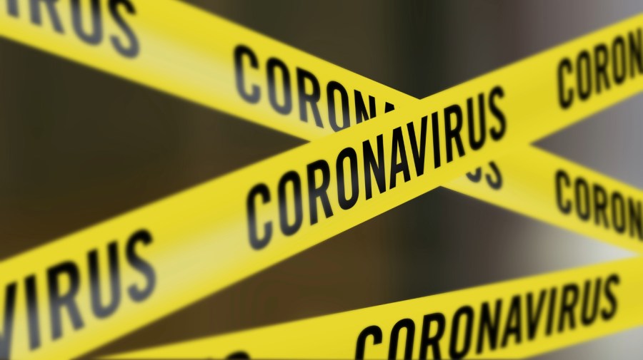 Yellow caution tape with the word coronavirus repeated is crisscrossed against a dark background.