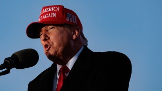 Former President Trump wears his iconic "Make America Great Again" red hat while speaking at an event.