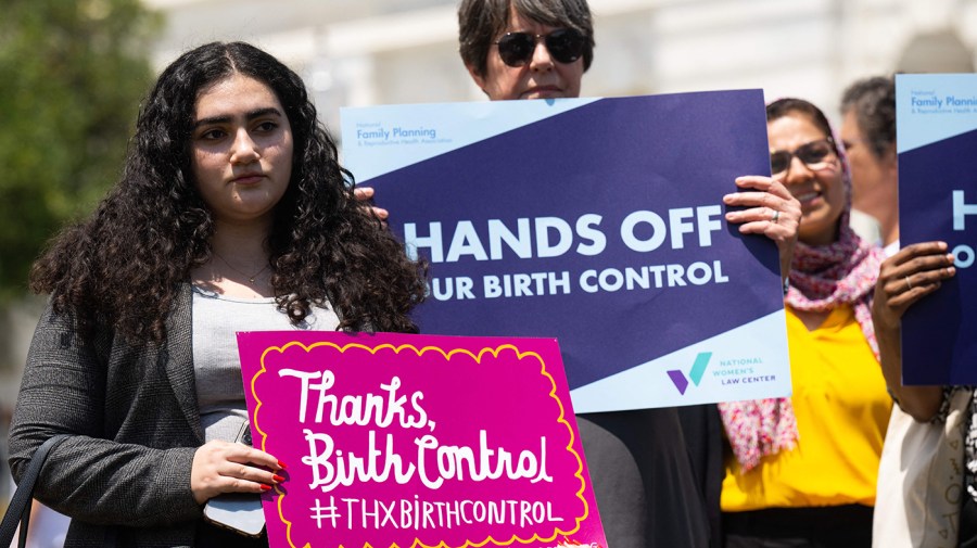 Reproductive-rights supporters hold signs saying "Hands off our birth control" and "Thanks, birth control" at an event.