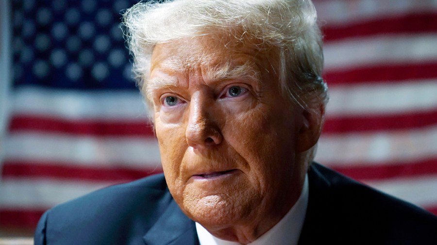 Former President Trump is seen in a close-up with a large American flag behind him.