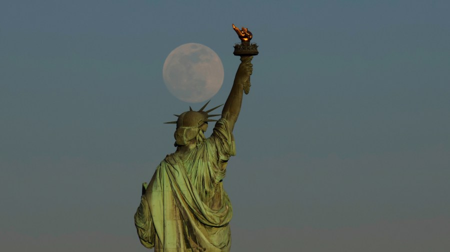 The Pink Moon, illuminated at 99 percent, rises behind the Statue of Liberty as the sun sets in New York City on April 22, 2024, as seen from Jersey City, New Jersey.