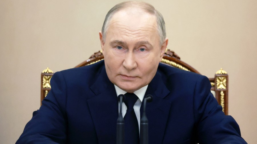 Russian President Vladimir Putin is seated at a meeting.