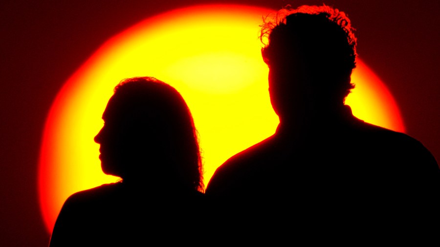 A couple watches the sun set from a park, July 10, 2021, in Kansas City, Mo.