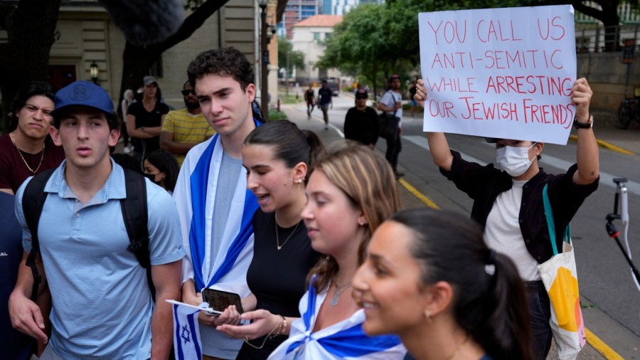 A Pro-Palestinian protester holds up a sign as Jewish students talk to the media following on campus at the University of Texas at Austin, Tuesday, April 30, 2024, in Austin, Texas.