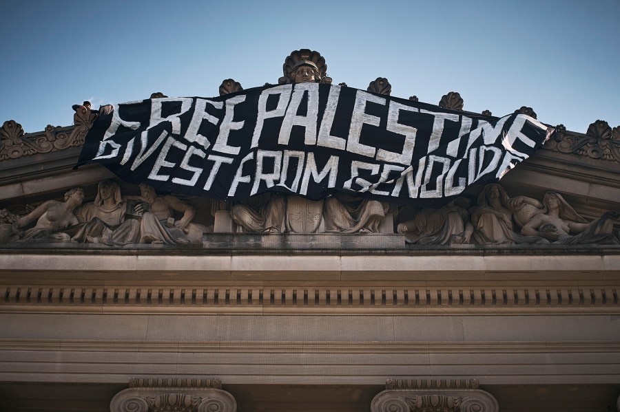 A pro-Palestinian demonstrator, upper left, hangs a flag on top of the Brooklyn Museum during a protest demanding a permanent cease-fire in Gaza, Friday, May 31, 2024, in New York. (AP Photo/Andres Kudacki)