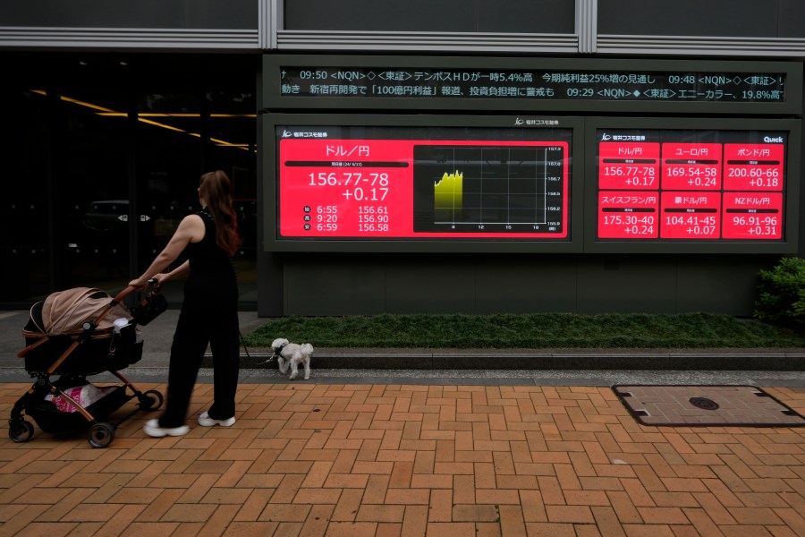 A woman walks her dog strolling past monitors showing Japan's foreign exchange rate against the U.S. dollar and other foreign currencies at a securities firm in Tokyo, Thursday, June 13, 2024. (AP Photo/Hiro Komae)