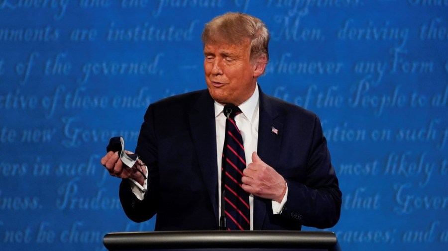 Then-President Trump looks at his face mask while on stage during a debate.