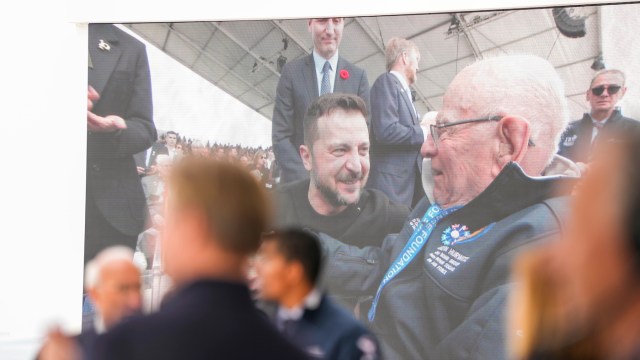 Ukrainian President Volodymyr Zelensky is seen on a screen meeting a veteran.