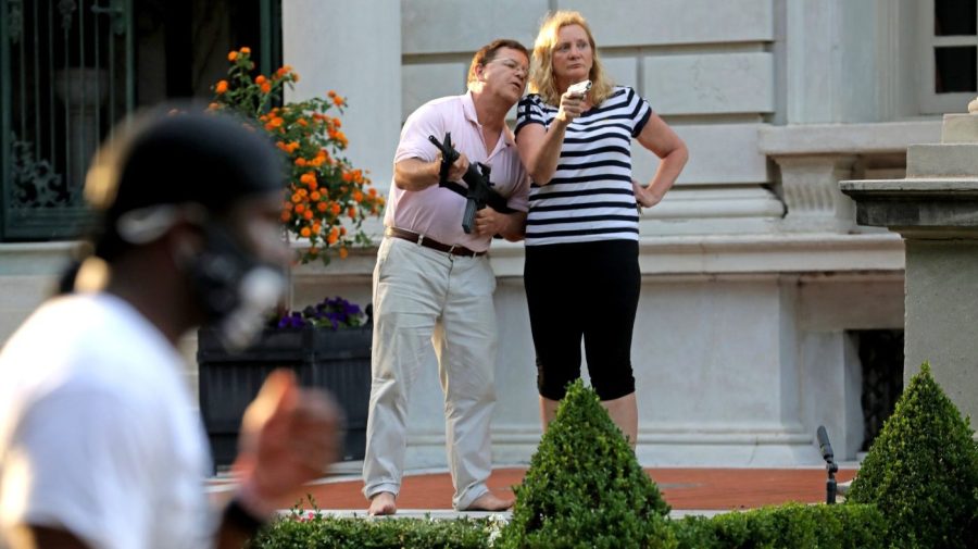 Mark and Patricia McCloskey stand armed in their front lawn as protesters walk past.