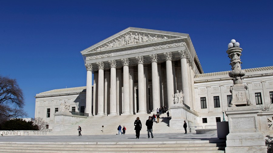 People walk up and down the steps to the Supreme Court on a bright, clear day.