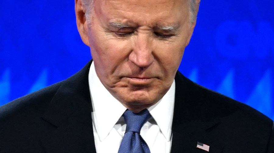 President Biden looks down in a close-up in front of a blue backdrop.