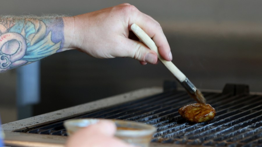 Chef Zach Tyndall brushes sauce on a piece of Good Meat's cultivated chicken as it cooks on a grill at the Eat Just office on July 27, 2023 in Alameda, California. (Photo by Justin Sullivan/Getty Images)