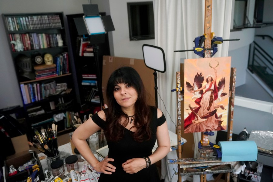 FILE - Artist Karla Ortiz poses next to one of her paintings, right, in San Francisco, Aug. 4, 2023. The version of the painting uploaded online belies a hidden defense system — a tool called Glaze that masks the artist's style and cloaks the art from use by generative AI. (AP Photo/Jeff Chiu, File)