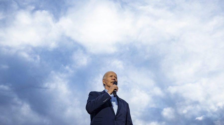 President Biden is seen from below against a cloudy blue sky.