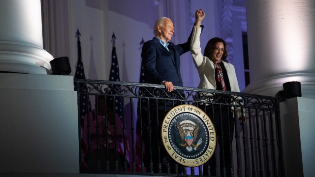 President Biden raises the arm of Vice President Harris on a balcony.