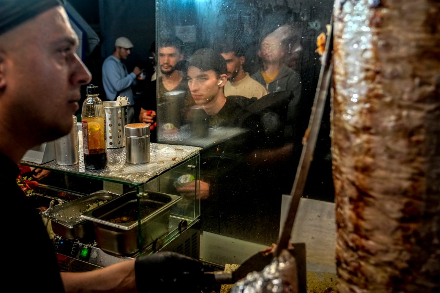 People stand in the line to buy doner kebab while the Turkish cook prepares the doner kebabs, in Berlin, Germany, Wednesday, Sept. 18, 2024. (AP Photo/Ebrahim Noroozi)