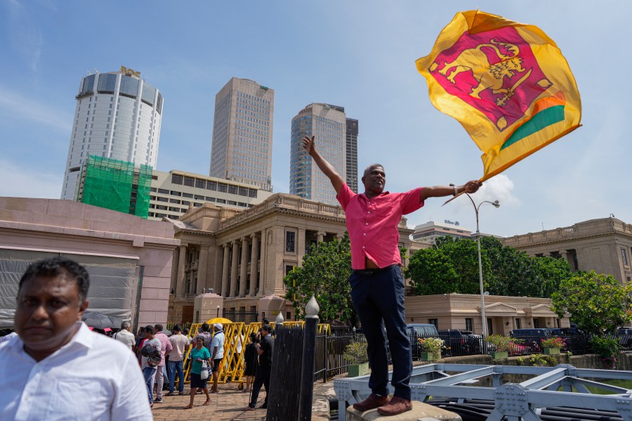 A supporter waves Sri Lankan flag as he waits for the swearing in ceremony of president elect Marxist lawmaker Anura Kumara Dissanayake out side president's office in Colombo, Sri Lanka, Monday, Sept. 23, 2024. (AP Photo/Eranga Jayawardena)