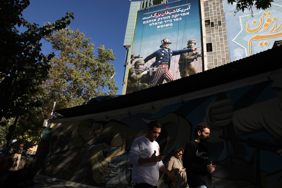 People walk under an anti-U.S. and anti-Israel banner with writing in Farsi reading: "America is the great Satan", and in Hebrew "America will throw you away like used toilet paper", at the Felestin (Palestine) Sq. in downtown Tehran, Iran, Wednesday, Nov. 6, 2024. (AP Photo/Vahid Salemi)