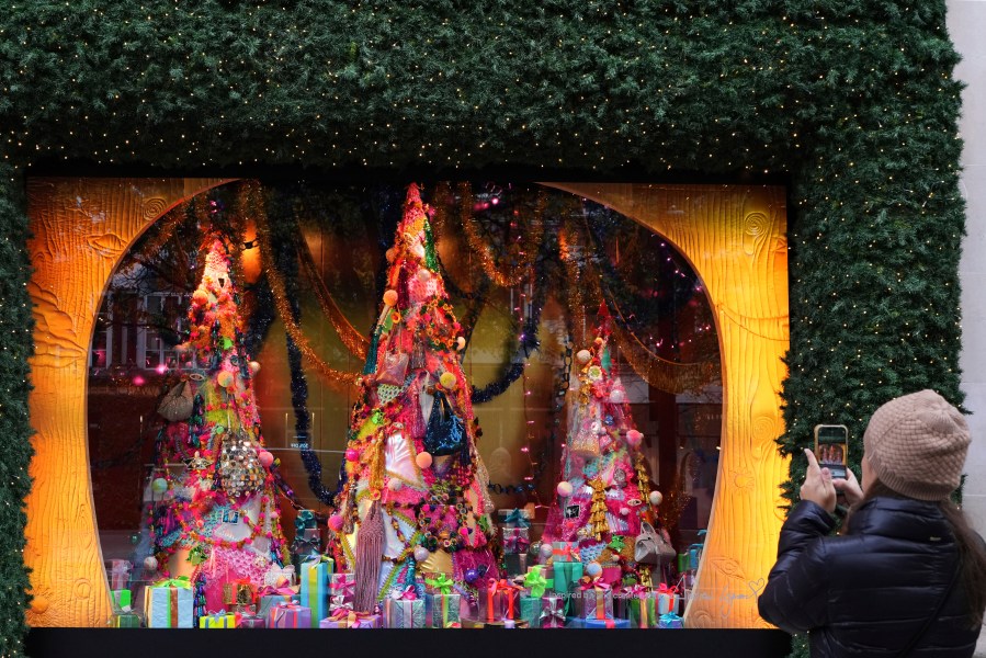 A woman photographs a festive shop window in Oxford Street in London, Friday, Nov. 15, 2024. (AP Photo/Kirsty Wigglesworth)