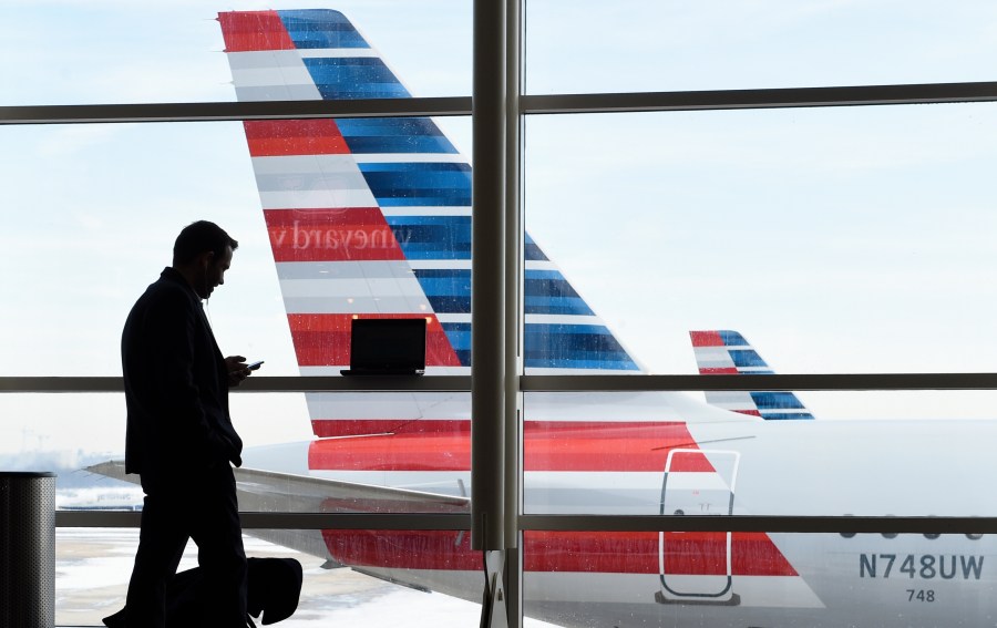 FILE - A passenger talks on the phone with American Airlines jets parked behind him at Washington's Ronald Reagan National Airport in Washington, Jan. 25, 2016. (AP Photo/Susan Walsh, File)